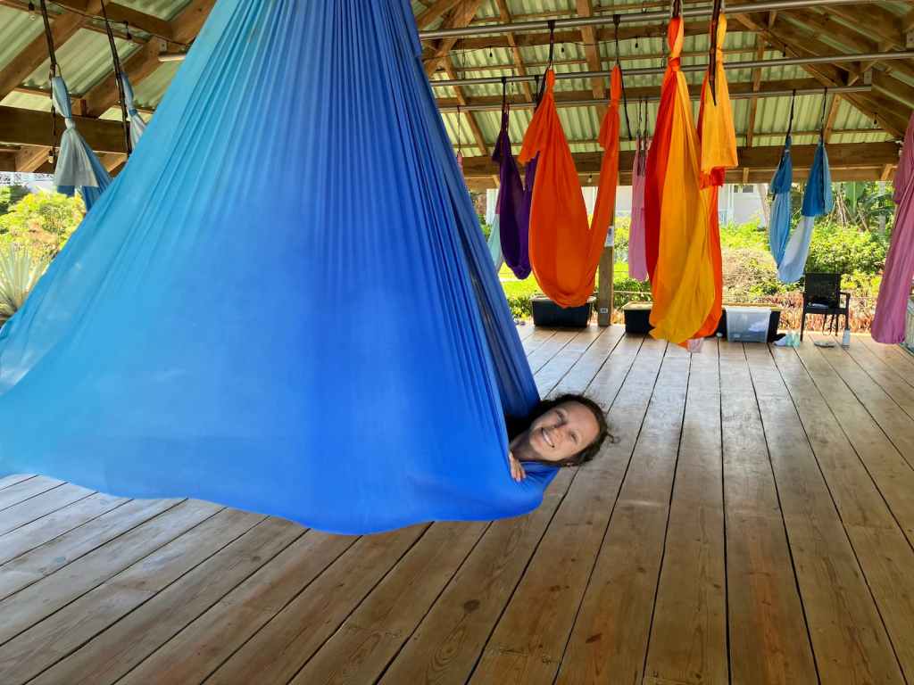 Kelsey lying down in blue aerial yoga hammock with head peeking out