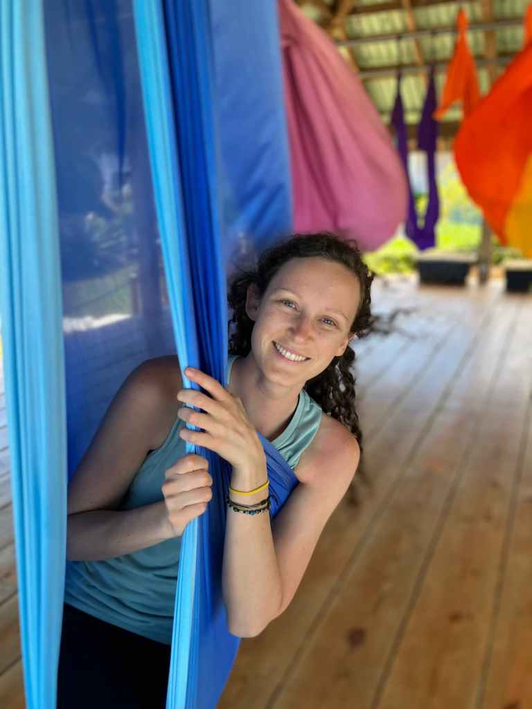 Kelsey smiling while holding onto blue aerial hammock