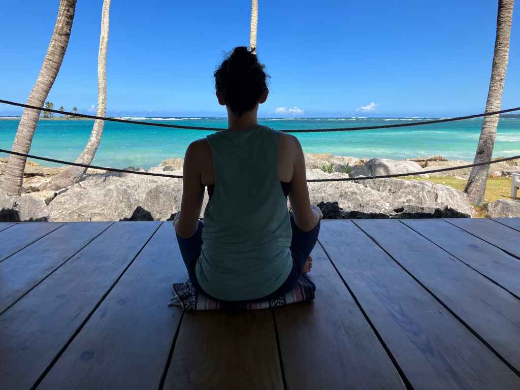Silhouette of Kelsey sitting in yoga shala with bright tropical ocean in background