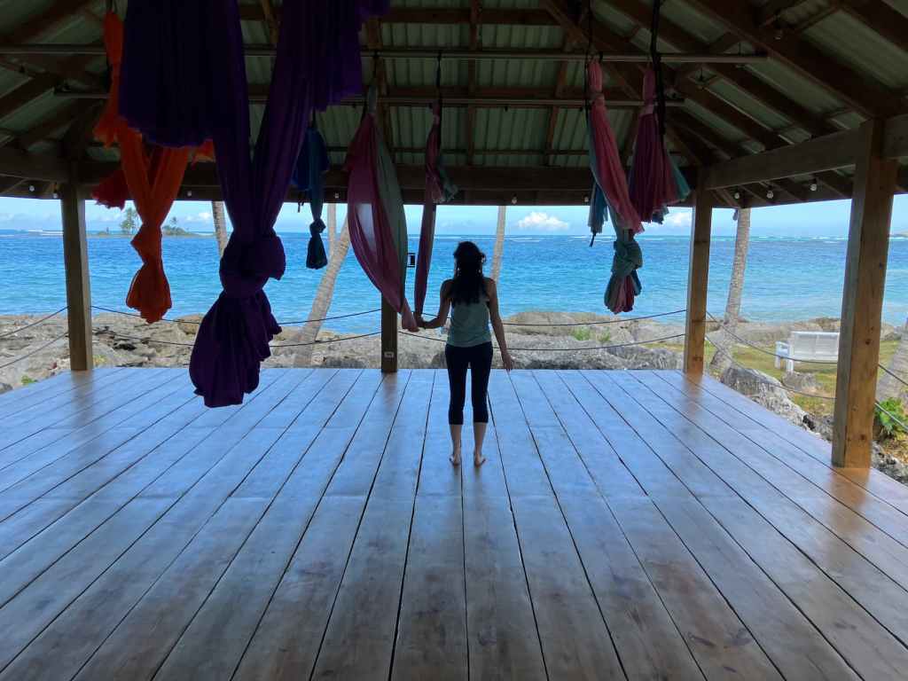 Silhouette of Kelsey standing in yoga shala holding aerial hammock