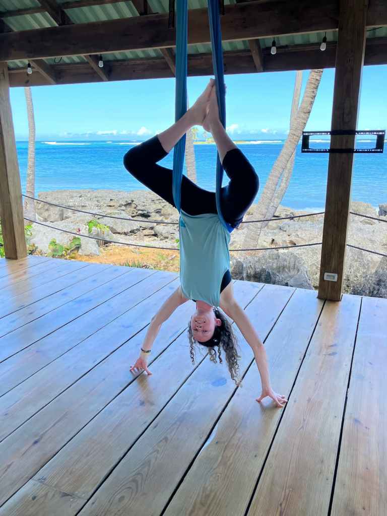 Kelsey hanging upside down in aerial hammock with hands on ground
