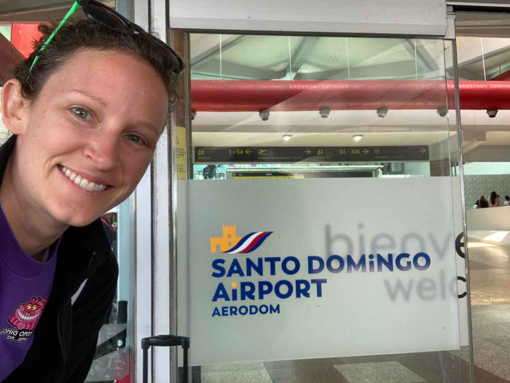 Kelsey next to Santo Domingo Airport logo on glass door